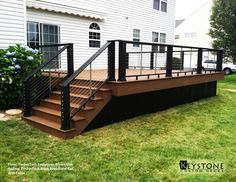 a deck with railing and handrails in front of a house on the grass