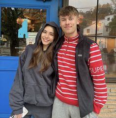 a young man and woman standing in front of a blue door smiling at the camera