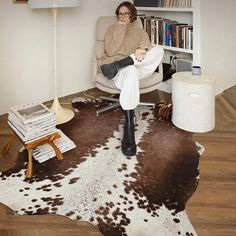 a woman sitting in a chair on top of a cowhide rug next to a lamp