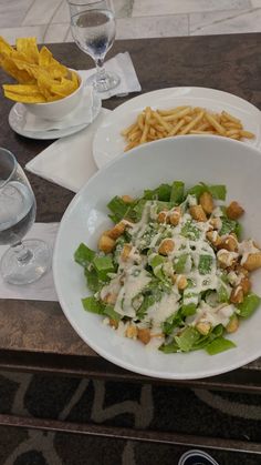 a salad and french fries are sitting on a table next to wine glasses, silverware, and water