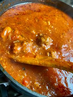 a wooden spoon in a pot full of food on the stove top, with meatballs and tomato sauce