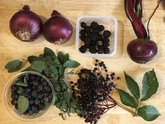 an assortment of fruits and vegetables on a wooden table with leaves, onions, berries, and other items