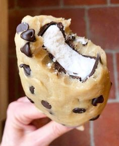 a person holding up a chocolate chip cookie doughnut with white frosting and chocolate chips