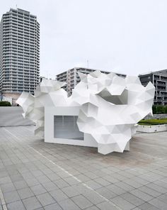 a white sculpture sitting on top of a cement floor next to tall buildings in the background