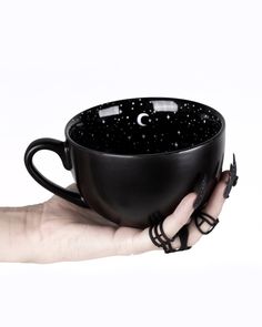 a woman's hand holding a black coffee cup with the moon and stars on it