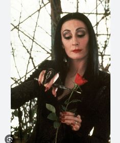 a woman holding a rose in her right hand and looking at the camera with an evil look on her face