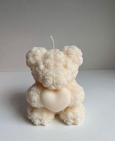 a white teddy bear with a heart shaped candle in the shape of a rosette