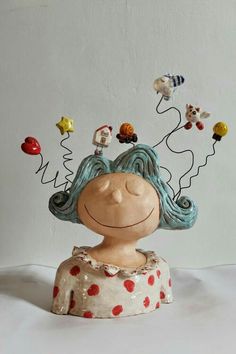 a ceramic sculpture of a woman's head with many small objects in the air