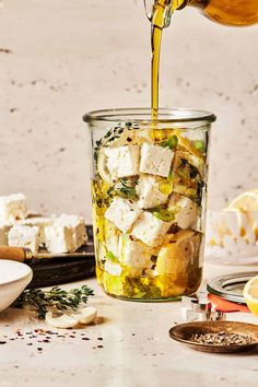 a person pouring dressing into a glass jar filled with tofu and vegetables next to sliced lemons