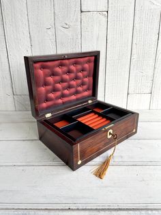 an open wooden box with red velvet lining and tassels on the inside, sitting on a white wood floor