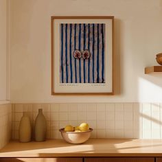 a bowl of fruit sitting on top of a kitchen counter next to a framed poster