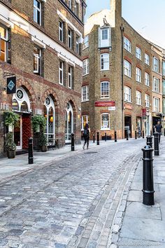 an empty brick street with people walking on the sidewalk and buildings in the back ground