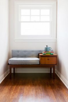 a wooden bench sitting in front of a window next to a table with books on it