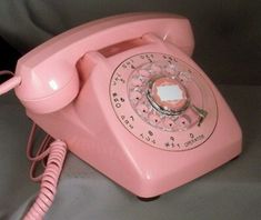 an old pink telephone sitting on top of a gray table next to a phone cord