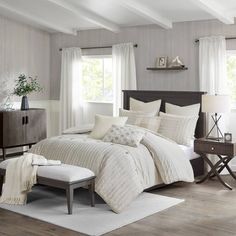 a bed sitting in a bedroom on top of a wooden floor next to two windows