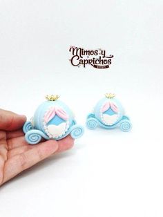 a hand is holding two miniature blue princess carriage earrings with pink bows on it's head