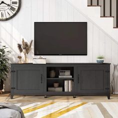 a flat screen tv sitting on top of a wooden cabinet in front of a stair case