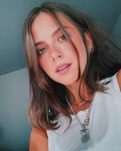 a woman wearing a white shirt with a necklace on her neck is posing for the camera