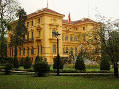 a large yellow building sitting in the middle of a lush green park next to trees