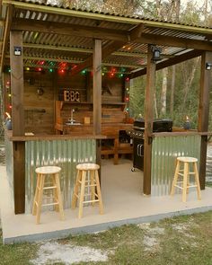 an outdoor bar with three stools and lights on the roof, surrounded by trees