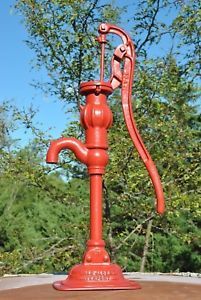 an old fashioned red water faucet sitting on top of a wooden table in front of some trees