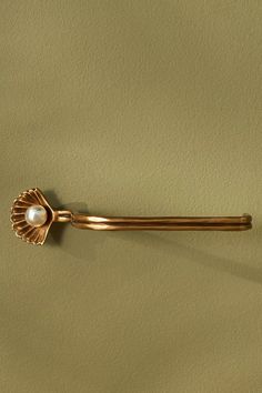 a gold tie bar with a pearl in the center on a green background, close up