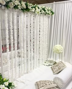 a white backdrop with flowers and beads hanging from it's sides, along with pillows on the floor