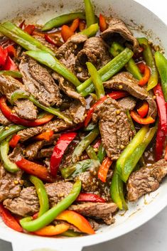 stir fry with beef and peppers in a skillet on a white counter top, ready to be eaten