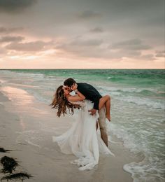 a bride and groom kissing on the beach in front of the ocean at sunset or sunrise