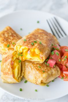 an omelet with eggs and tomatoes on a white plate next to a fork