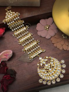 some gold jewelry is laying on top of a wooden table with flowers and other accessories