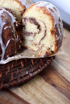 a cinnamon roll is cut in half on a wooden cutting board next to a basket