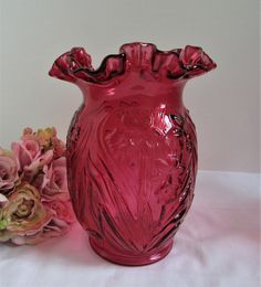 a pink vase sitting on top of a white table next to some flowers and leaves