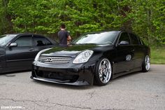 two black cars parked next to each other in front of some green trees and bushes