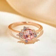 a pink diamond ring sitting on top of a white table next to a beige cloth