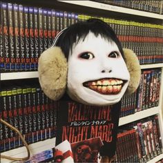 a creepy mask with ear muffs hanging from it's side in front of a book shelf