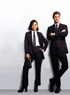 two business people standing next to each other in front of a white wall with their arms crossed