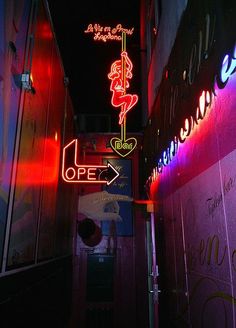 an alleyway at night with neon signs and graffiti on the walls, including one sign that says open