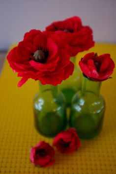 three vases with red flowers in them on a yellow table