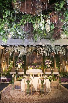 an elaborate table and chairs are set up for a formal function with greenery hanging from the ceiling