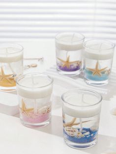 four candles with seashells and starfish in them sitting on a white table