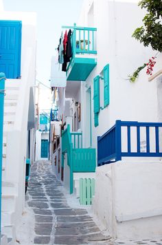 an alley way with blue and white buildings on either side, and clothes hanging from balconies