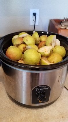 a crock pot filled with apples and pears sitting on a counter next to an outlet