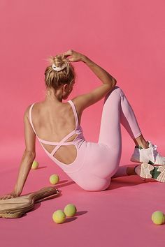 a woman sitting on the ground with tennis balls in front of her and wearing a pink leotard