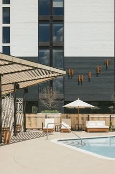 an outdoor swimming pool with lounge chairs and umbrellas next to it in front of a large building