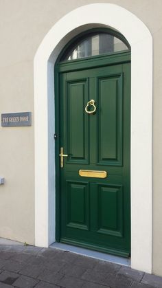 a green door with a gold handle on the side of a building that has a white arch above it