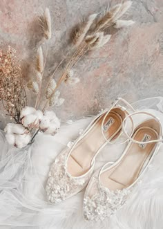 a pair of white shoes sitting on top of a bed next to dried flowers and feathers