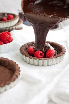 chocolate tart pies with raspberries being drizzled over them