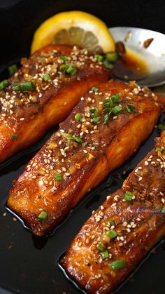 salmon fillets with sesame seeds and lemon wedges on a black plate next to a spoon