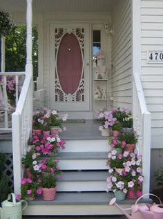 a white house with pink flowers on the front porch and steps leading up to it